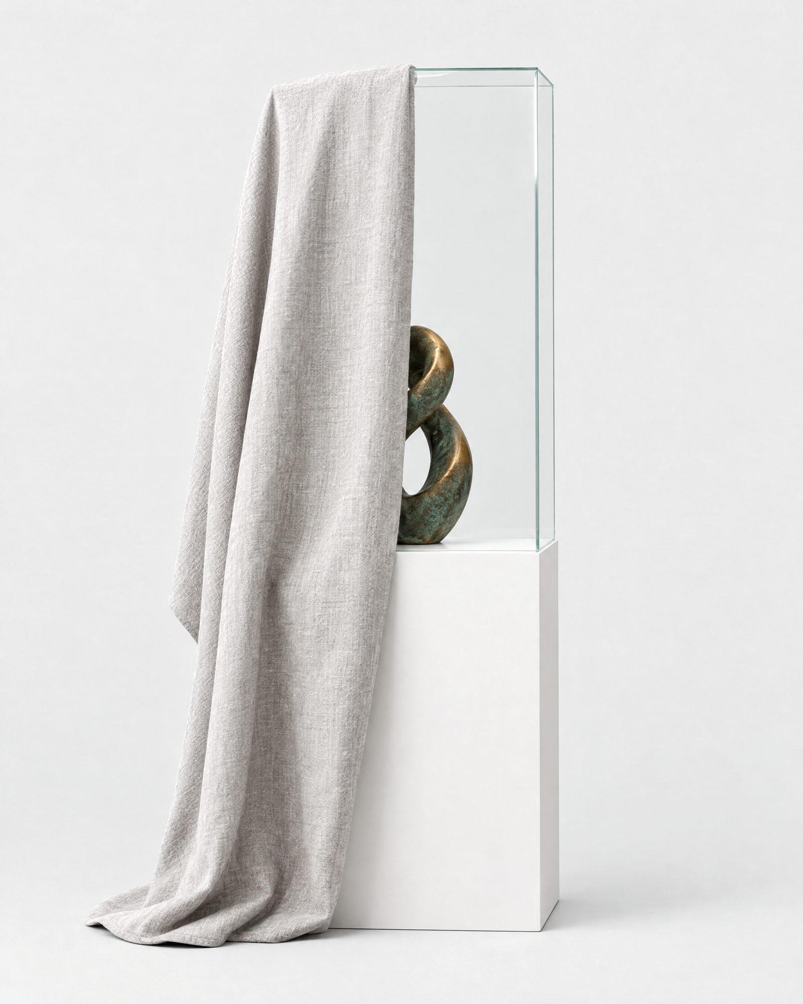A green-patinated bronze sculpture in a glass vitrine, half covered by a pale grey linen cloth
